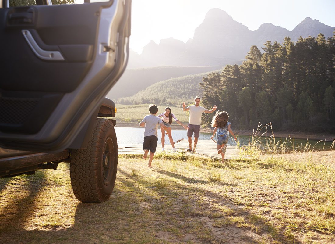 About Our Agency - Excited Family Reaching Countryside Destination on a Road Trip at Sunset