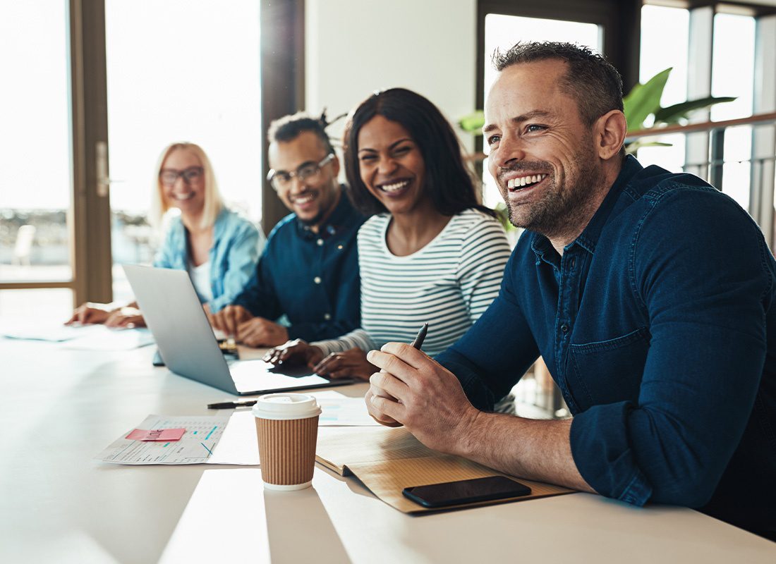 Insurance Solutions - Business Colleagues Smiling in Laughing While Working in a Large Conference Room of Their Modern Office